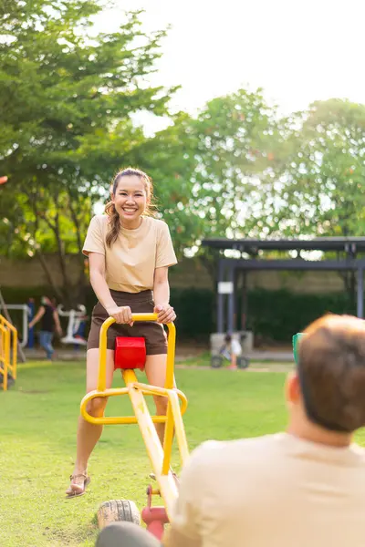 Asian couple love play seesaw with smiling in kids playground