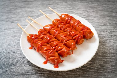 Beyaz tabakta ketçaplı kızarmış sosis şişi.