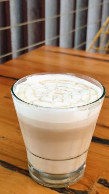 Ahşap bir masada servis edilen üzerinde çiçek resmi olan bal karamel latte..