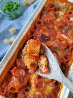 Baked rigatoni casserole with tomato sauce, bell peppers, peas, and melted mozzarella cheese in a cream-colored rectangular baking dish clipart