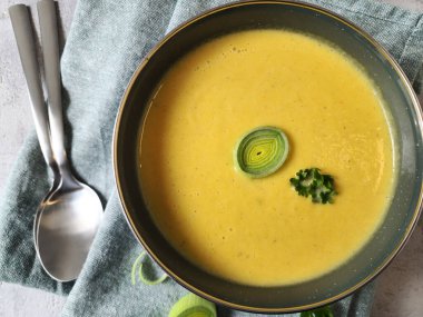 Çedar peynirli kremalı pırasa çorbası, pırasa halkaları ve maydanozla süslenmiş.