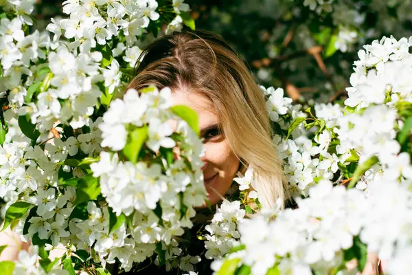 Parkta duran genç sarışın kadın baharda beyaz çiçeklerle çiçek açmış bir elma ağacında. Yüksek kalite fotoğraf