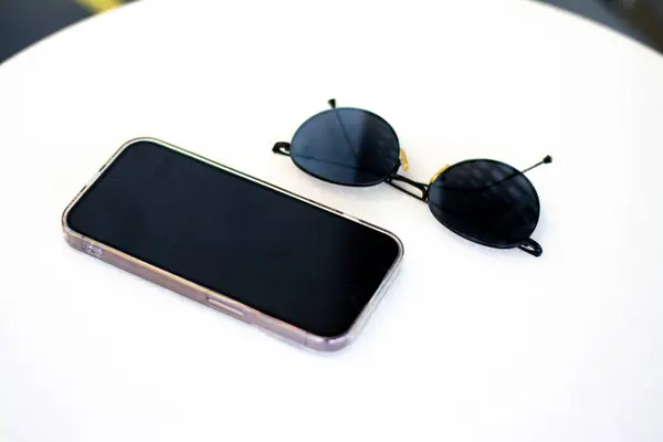 Beyaz arkaplanda güneş gözlüklü akıllı telefon