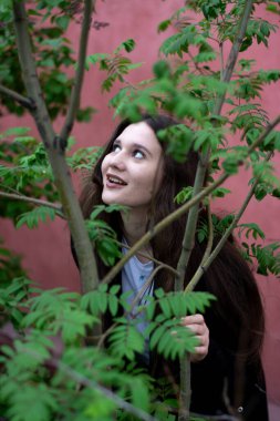 Bahçede poz veren uzun saçlı genç bir kadının portresi.