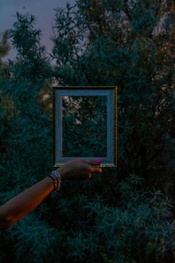 Sahilde aynalı siyah bir çerçeve tutan bir kadın silueti.