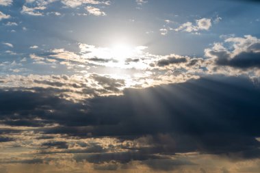 Güneş mavi gökyüzündeki karanlık bulutların arasından parlıyor. Gökyüzünün arkaplanı.