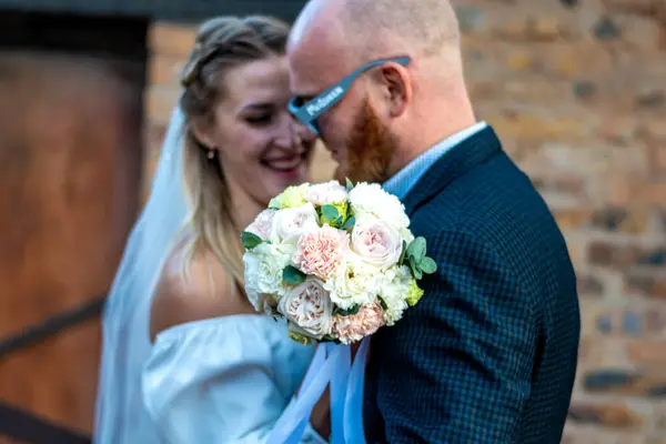 Gelin ve damat, duvarın önünde düğün buketi tutuyorlar.