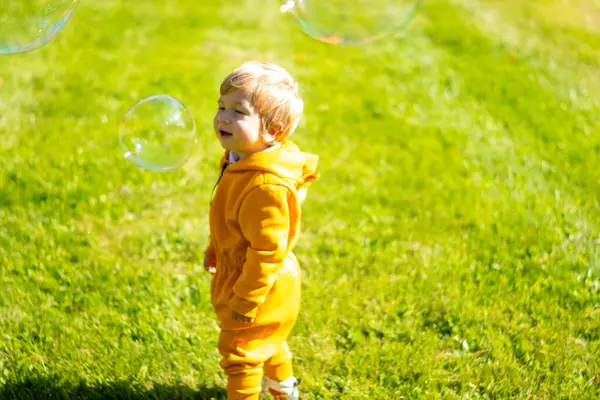 Küçük çocuk sabun köpüğüyle yeşil çimlerde oynuyor..