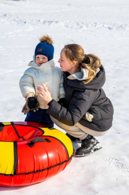 Mavi ceketli genç anne ve oğlu ve kışın gölde oyuncak taşıyan sarı ceketli.