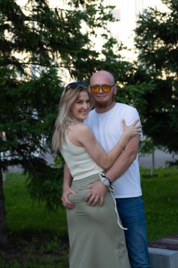 Beyaz tişörtlü, kot pantolonlu, yeşil arka planda poz veren güzel sarışın bir kadının portresi..