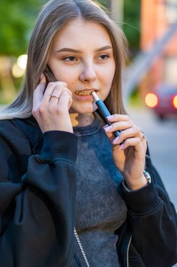 Sokakta e-sigara içen genç bir kadın telefonda konuşuyor. Bağımlılık konsepti. Yüksek kalite fotoğraf. Yüksek kalite fotoğraf