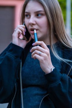 Sokakta e-sigara içen genç bir kadın telefonda konuşuyor. Bağımlılık konsepti. Yüksek kalite fotoğraf. Yüksek kalite fotoğraf