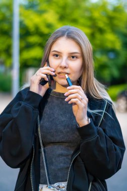Sokakta e-sigara içen genç bir kadın telefonda konuşuyor. Bağımlılık konsepti. Yüksek kalite fotoğraf. Yüksek kalite fotoğraf