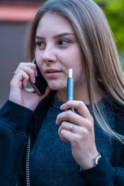 Sokakta e-sigara içen genç bir kadın telefonda konuşuyor. Bağımlılık konsepti. Yüksek kalite fotoğraf. Yüksek kalite fotoğraf