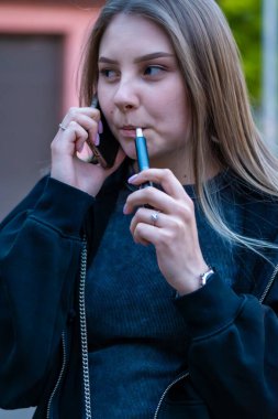 Sokakta e-sigara içen genç bir kadın telefonda konuşuyor. Bağımlılık konsepti. Yüksek kalite fotoğraf. Yüksek kalite fotoğraf