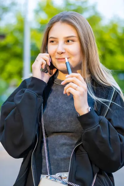 Sokakta e-sigara içen genç bir kadın telefonda konuşuyor. Bağımlılık konsepti. Yüksek kalite fotoğraf. Yüksek kalite fotoğraf
