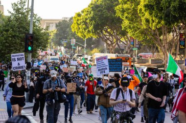 Muhtelif protestoculardan oluşan geniş bir kalabalık Los Angeles şehir merkezinde anti-ICE ve Trump karşıtı levhalarla Meksika ve Amerikan bayrakları sallayarak toplanıyor. Siyasi gösteri, göçmen hakları, sosyal adalet ve toplumsal dayanışmayı destekliyor. Fotoğraflı dur