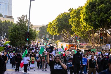 Muhtelif protestoculardan oluşan geniş bir kalabalık Los Angeles şehir merkezinde anti-ICE ve Trump karşıtı levhalarla Meksika ve Amerikan bayrakları sallayarak toplanıyor. Siyasi gösteri, göçmen hakları, sosyal adalet ve toplumsal dayanışmayı destekliyor. Fotoğraflı dur