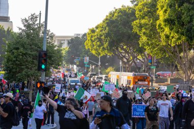 Muhtelif protestoculardan oluşan geniş bir kalabalık Los Angeles şehir merkezinde anti-ICE ve Trump karşıtı levhalarla Meksika ve Amerikan bayrakları sallayarak toplanıyor. Siyasi gösteri, göçmen hakları, sosyal adalet ve toplumsal dayanışmayı destekliyor. Fotoğraflı dur