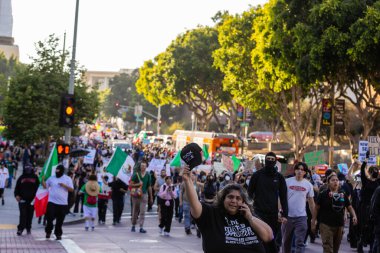 Muhtelif protestoculardan oluşan geniş bir kalabalık Los Angeles şehir merkezinde anti-ICE ve Trump karşıtı levhalarla Meksika ve Amerikan bayrakları sallayarak toplanıyor. Siyasi gösteri, göçmen hakları, sosyal adalet ve toplumsal dayanışmayı destekliyor. Fotoğraflı dur
