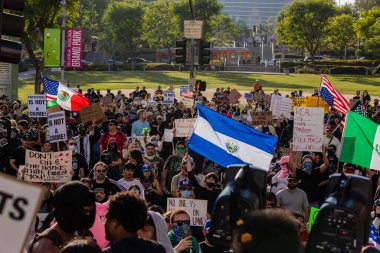 Muhtelif protestoculardan oluşan geniş bir kalabalık Los Angeles şehir merkezinde anti-ICE ve Trump karşıtı levhalarla Meksika ve Amerikan bayrakları sallayarak toplanıyor. Siyasi gösteri, göçmen hakları, sosyal adalet ve toplumsal dayanışmayı destekliyor. Fotoğraflı dur