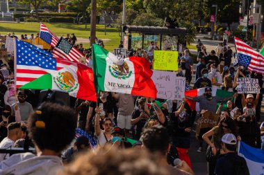 Muhtelif protestoculardan oluşan geniş bir kalabalık Los Angeles şehir merkezinde anti-ICE ve Trump karşıtı levhalarla Meksika ve Amerikan bayrakları sallayarak toplanıyor. Siyasi gösteri, göçmen hakları, sosyal adalet ve toplumsal dayanışmayı destekliyor. Fotoğraflı dur