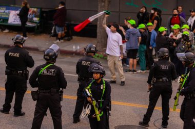 Muhtelif protestoculardan oluşan geniş bir kalabalık Los Angeles şehir merkezinde anti-ICE ve Trump karşıtı levhalarla Meksika ve Amerikan bayrakları sallayarak toplanıyor. Siyasi gösteri, göçmen hakları, sosyal adalet ve toplumsal dayanışmayı destekliyor. Fotoğraflı dur