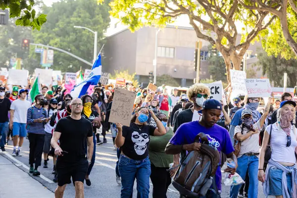 Muhtelif protestoculardan oluşan geniş bir kalabalık Los Angeles şehir merkezinde anti-ICE ve Trump karşıtı levhalarla Meksika ve Amerikan bayrakları sallayarak toplanıyor. Siyasi gösteri, göçmen hakları, sosyal adalet ve toplumsal dayanışmayı destekliyor. Fotoğraflı dur