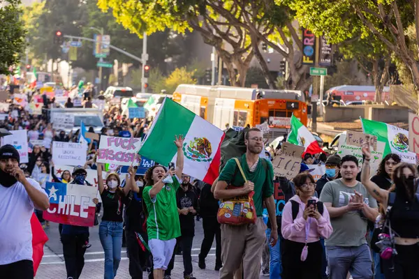 Muhtelif protestoculardan oluşan geniş bir kalabalık Los Angeles şehir merkezinde anti-ICE ve Trump karşıtı levhalarla Meksika ve Amerikan bayrakları sallayarak toplanıyor. Siyasi gösteri, göçmen hakları, sosyal adalet ve toplumsal dayanışmayı destekliyor. Fotoğraflı dur