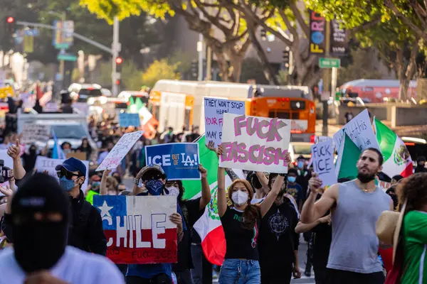 Muhtelif protestoculardan oluşan geniş bir kalabalık Los Angeles şehir merkezinde anti-ICE ve Trump karşıtı levhalarla Meksika ve Amerikan bayrakları sallayarak toplanıyor. Siyasi gösteri, göçmen hakları, sosyal adalet ve toplumsal dayanışmayı destekliyor. Fotoğraflı dur