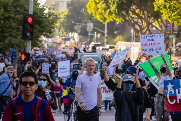 Muhtelif protestoculardan oluşan geniş bir kalabalık Los Angeles şehir merkezinde anti-ICE ve Trump karşıtı levhalarla Meksika ve Amerikan bayrakları sallayarak toplanıyor. Siyasi gösteri, göçmen hakları, sosyal adalet ve toplumsal dayanışmayı destekliyor. Fotoğraflı dur