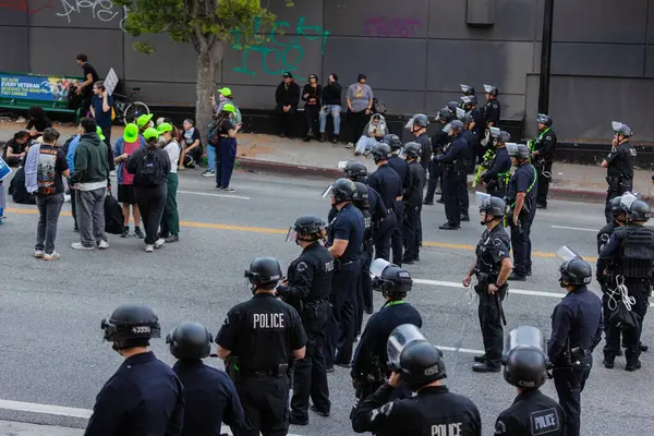 Muhtelif protestoculardan oluşan geniş bir kalabalık Los Angeles şehir merkezinde anti-ICE ve Trump karşıtı levhalarla Meksika ve Amerikan bayrakları sallayarak toplanıyor. Siyasi gösteri, göçmen hakları, sosyal adalet ve toplumsal dayanışmayı destekliyor. Fotoğraflı dur