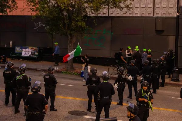 Muhtelif protestoculardan oluşan geniş bir kalabalık Los Angeles şehir merkezinde anti-ICE ve Trump karşıtı levhalarla Meksika ve Amerikan bayrakları sallayarak toplanıyor. Siyasi gösteri, göçmen hakları, sosyal adalet ve toplumsal dayanışmayı destekliyor. Fotoğraflı dur