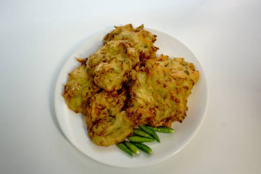 Selective focus Bakwan sayur or Bakwan Goreng or bala-bala or ote-ote is vegetebles fritter from Indonesia, served with cayenne peppers on white plate. clipart
