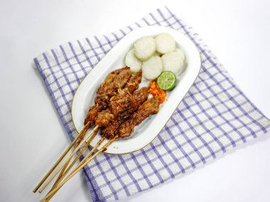 Fıstık soslu Sate Ayam (Tavuk satay) ve lontong (pirinç keki). Endonezya 'nın popüler sokak yemeklerinden biri. Beyaz masada beyaz tabakta servis ediliyor. Seçici odak.