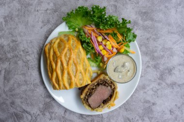 Ev yapımı sığır eti Wellington, ahşap tabakta salata ve mantar sosuyla servis edilen fileto tabağı.
