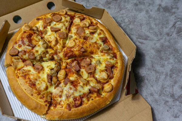 Freshly baked american pan pizza with a lot of cheese, chicken sausage, thin and crispy kebab meat on a board, take-away dish