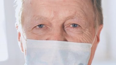 Koronavirüs salgınından korunmak için yüzüne tıbbi maske takan yaşlı bir adamın yakın plan portresi. Hastanede koruyucu maske takan bir adam.. 