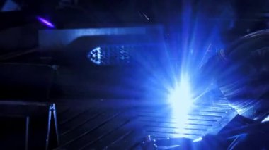 Fabrika işçisi metali kaynaklıyor. Adam kaynak yapıyor. Kaynak makinesi kullanarak argon veya elektrot ile kaynak yapmak. Metal yapılar üreten bir endüstriyel girişim. Kıvılcımlar ve parıltılar uçuşuyor. 