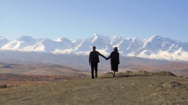  Dağlarda bir çift. Siyah elbiseli bir adam ve bir kadın, dağ uçurumuna doğru yürüyorlar. Arkaplan karla kaplı dağlara karşı. Mutlu bir aile.. 
