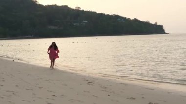 Bir kadın plaj boyunca koşuyor. İnce kadın bacakları ve ayakları kumlu bir sahilde kumların üzerinde yürüyor. Pembe elbiseli güzel kadın deniz sörfünde yürüyor.. 