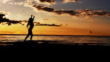 Gün batımında sahilde yürüyen bir kadın. Gün batımında suda yürüyen bir kızın silueti. Gün batımında denizde bir kız. Gün batımında ayaktan su damlaları.