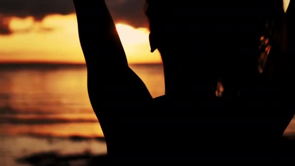 少女はビーチで日没時に髪をまっすぐにする 日没時のスレンダーガールのシルエット 海の夕日 クローズアップ — ストック動画