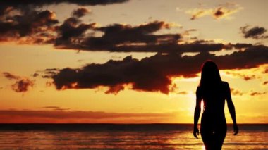 Gün batımında sahilde yürüyen bir kadın. Sahilden suya giren bir kızın silueti. Gün batımında denizde bir kız.