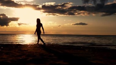 Gün batımında sahilde yürüyen bir kadın. Gün batımında suda yürüyen bir kızın silueti. Gün batımında denizde bir kız.