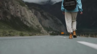 Doğadaki doğa gezgini konsepti. Dağlarda yol boyunca yürüyen bir kadının arka görüntüsü. Sırt çantasıyla yolda yürüyen bir kadın turist..