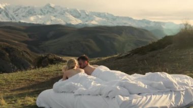 Birbirine aşık genç bir çift dağlarda bir battaniyeye uzanıyor, konuşuyor, karlı dağların ve birbirlerinin manzarasının tadını çıkarıyor..