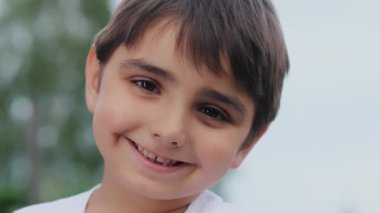 Gülümseyen bir çocuğun yakın plan portresi. Çocuk caddede gülümsüyor. Kameraya bakıp gülümseyen küçük bir çocuğun portresi. Küçük, güzel bir çocuğun yüzü. Mutlu küçük çocuk.