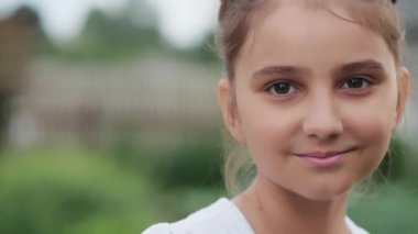 Gülümseyen bir kızın yakın plan portresi. Kız caddede gülümsüyor. Kameraya bakıp gülümseyen küçük bir kızın portresi. Küçük, güzel bir çocuğun yüzü. Mutlu küçük çocuk.