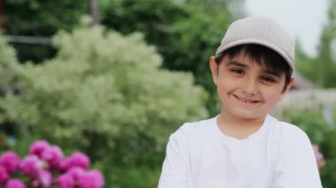 Şapkalı gülümseyen bir çocuğun yakın plan portresi. Çocuk caddede gülümsüyor. Kameraya bakıp gülümseyen küçük bir çocuğun portresi. Küçük, güzel bir çocuğun yüzü. Mutlu küçük çocuk.